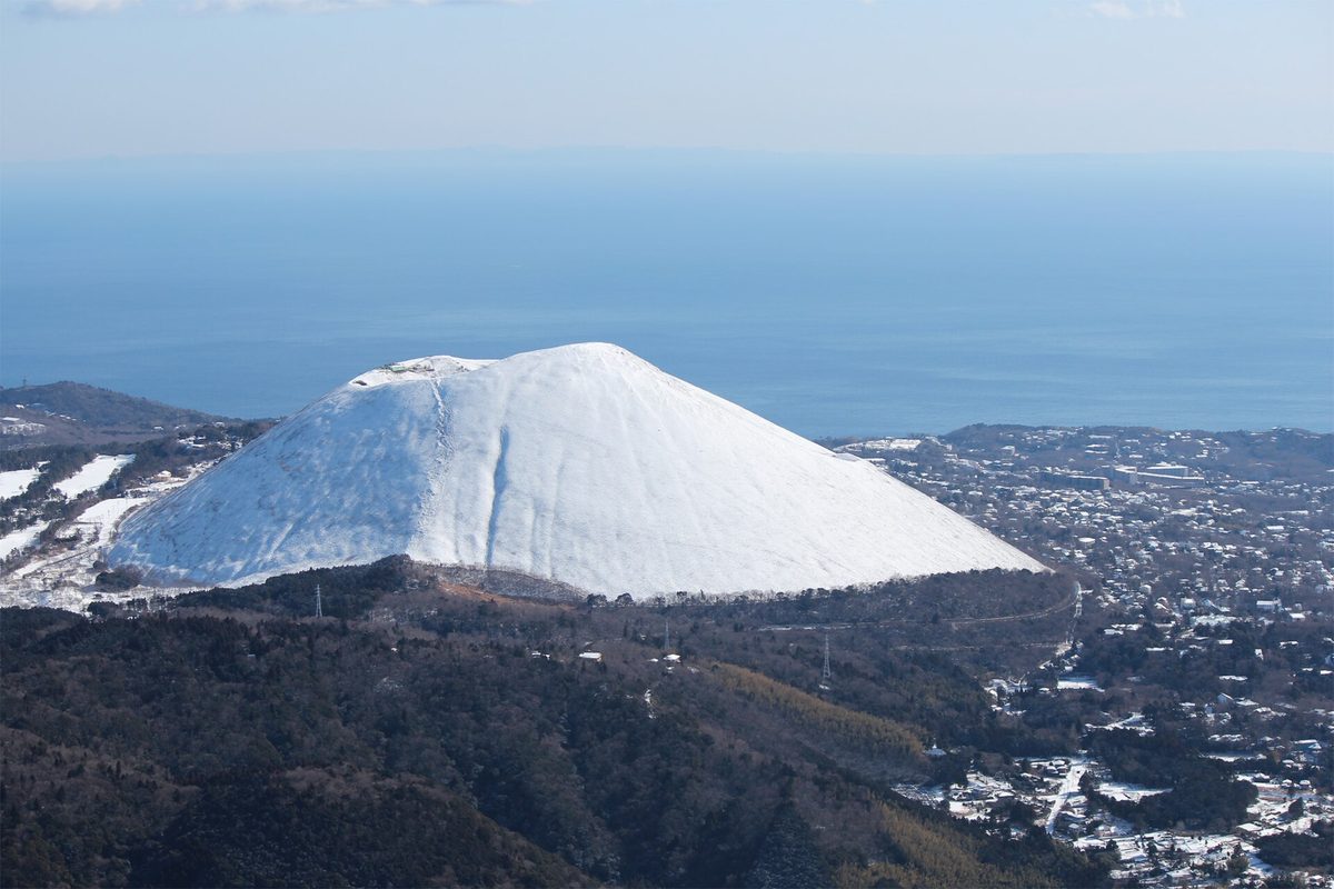 從西側山上遠望整座被白雪蓋住的大室山,山坡上的草完全看不見,右邊伊豆高原的屋頂也積著雪,背後是藍色的相模灘