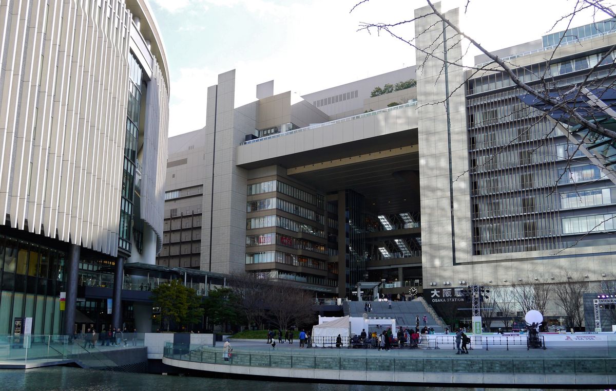 從うめきた広場的水池邊看大阪站北側:左邊是 Grand Front 大阪南館的白色直條紋弧形外牆,正面是 North Gate Building 中央的大開口與通往車站的大階梯,階梯旁的牆面有「大阪駅 OSAKA STATION」字樣
