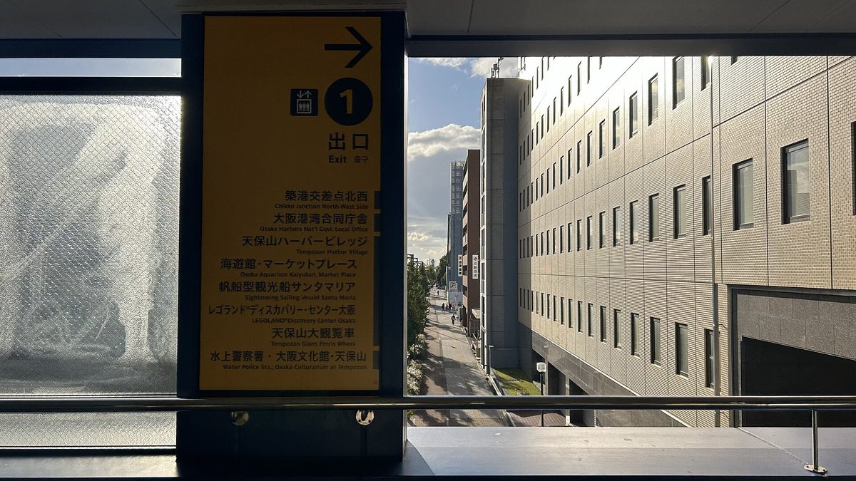 大阪港站站內的黃色指標,箭頭向右、大字「1 出口」,下面逐行列出築港交差点北西、天保山ハーバービレッジ、海遊館・マーケットプレース、帆船型観光船サンタマリア、レゴランド、天保山大観覧車等目的地,左上有電梯符號