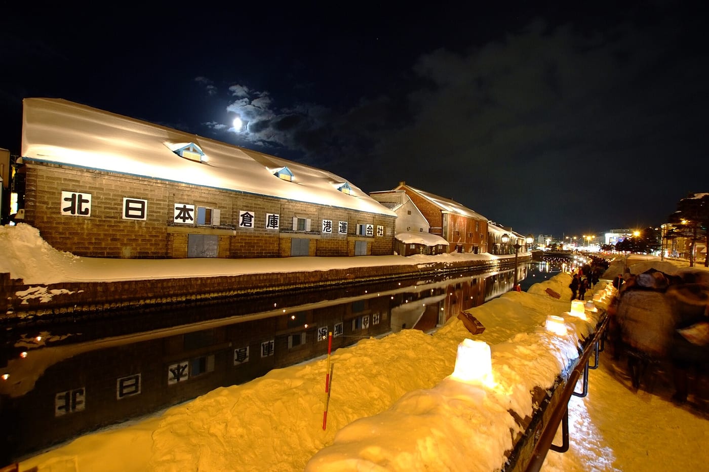 Otaru Snow Light Path: snow-covered stone warehouses lit at night along the canal, with candle snow-lanterns lining the walkway