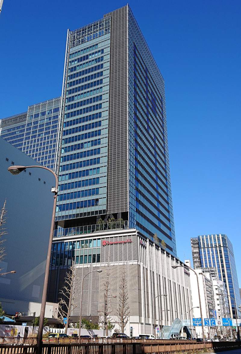從昭和通看日本橋高島屋 S.C. 東館:灰白色直條格柵的低層部,外牆有紅色的 Takashimaya S.C. 字樣,上方是藍綠色玻璃帷幕的高樓,右下有一座淺藍色的人行天橋
