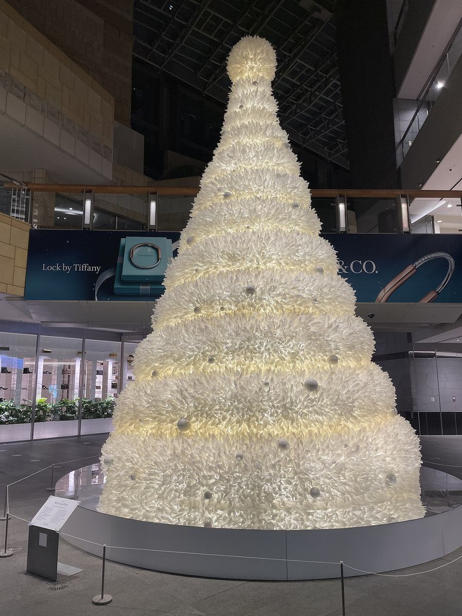 A white Christmas tree in the Roppongi Hills West Walk atrium, built as a cone of layered white feather-like material, with a rope barrier around its base