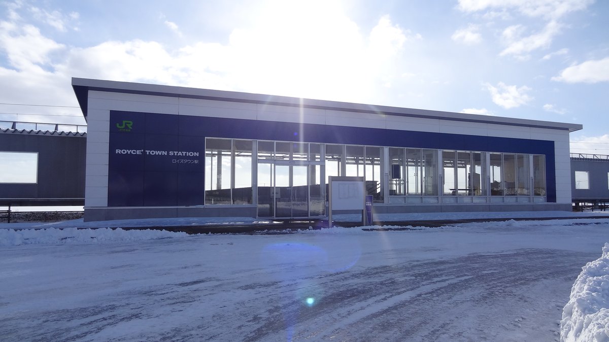 冬天的ロイズタウン站站房，深藍色外牆寫 ROYCE' TOWN STATION 與ロイズタウン駅，整面玻璃門窗，站前廣場的路面被壓實的積雪覆蓋，右邊堆著鏟起來的雪