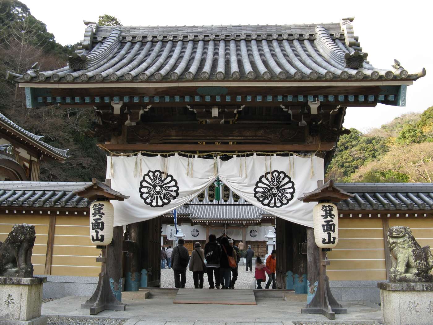 瀧安寺山門，白色暖簾印著寺紋，兩側掛著寫有「箕面山」的大燈籠，門前左右各一尊石造狛犬