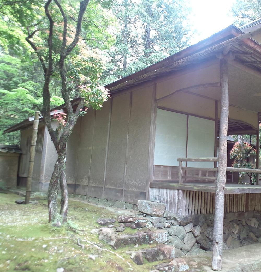 西芳寺下段庭園裡的茶室湘南亭:土牆與紙門的低矮建築,外側有木造緣側與竹編腰板,前方是苔地與石階,旁邊一棵楓樹