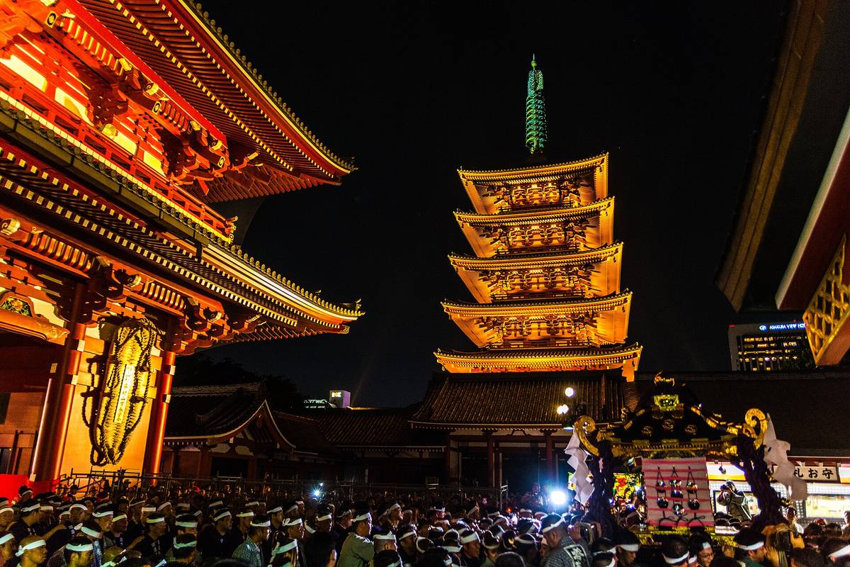 夜晚打燈的淺草寺寶藏門與五重塔，畫面下緣是一整排綁白色頭巾的人，右下角一座神輿被扛在人群上方