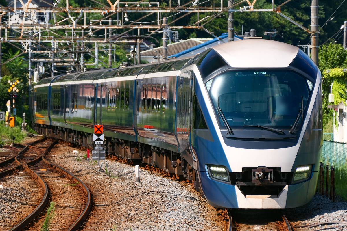 SAPHIR 踴子號沿著彎道駛進伊東站:深藍色車身、擋風玻璃上方顯示 RS1,左邊有分岔的鐵軌與號誌,上方是密集的架空電車線
