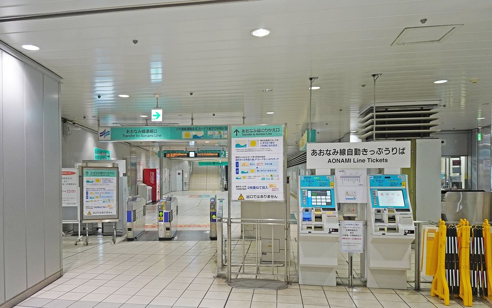 JR 名古屋站內通往青波線的連絡改札:上方綠色招牌寫「あおなみ線連絡口 Transfer to Aonami Line」,改札前立著「あおなみ線のりかえ口」的說明看板,用圖示說明交通系 IC 卡只要感應一張、磁氣車票要兩張重疊投入,右邊是兩台「あおなみ線自動きっぷうりば」售票機,售票機中間貼著寫有 6 時 00 分〜23 時 00 分的使用時間告示