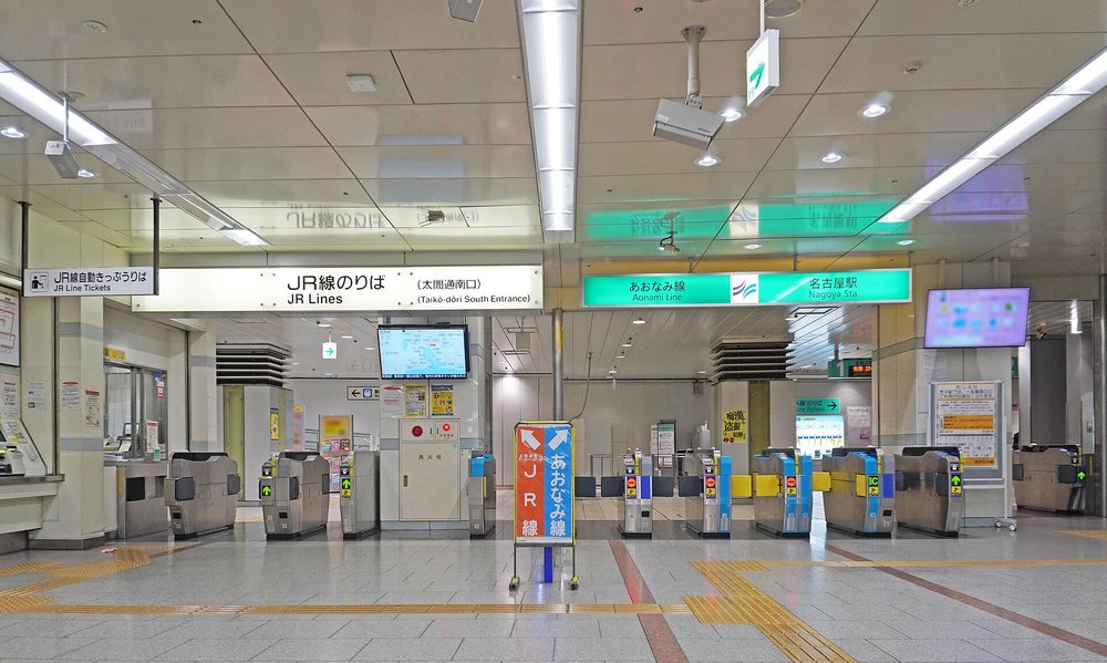 名古屋站太閤通南口的地下改札區:左半邊上方掛著白底黑字「JR線のりば(太閤通南口)」,右半邊上方是綠底「あおなみ線 名古屋駅」招牌,兩邊各有一排自動改札機,中間立著一塊左橘右藍、寫著「JR線」「あおなみ線」並畫有箭頭的指示看板