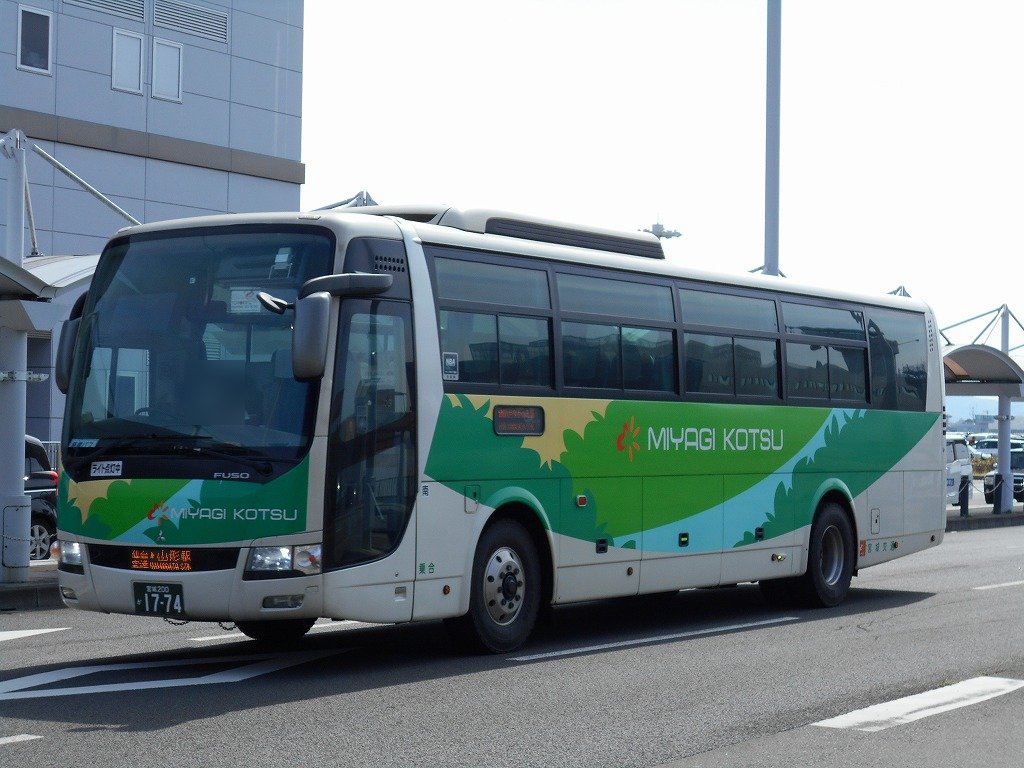 一輛銀白色車身、側面有綠色與水藍色波浪塗裝的高速巴士停在仙台機場航廈旁，車身寫著「MIYAGI KOTSU」，車頭下方的橘色字幕顯示往山形站的路線，背景是航廈的灰色外牆與遮雨棚
