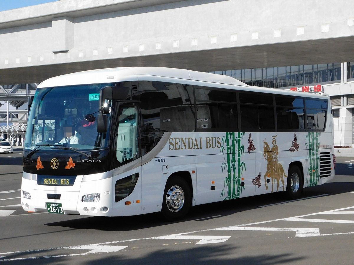 一輛白色大型遊覽巴士開在仙台機場航廈前的車道上，車身側面是金色「SENDAI BUS」字樣和綠色竹子、騎馬武將的圖案，車頭下方也寫著 SENDAI BUS，背景是航廈的混凝土外牆與一塊紅字招牌