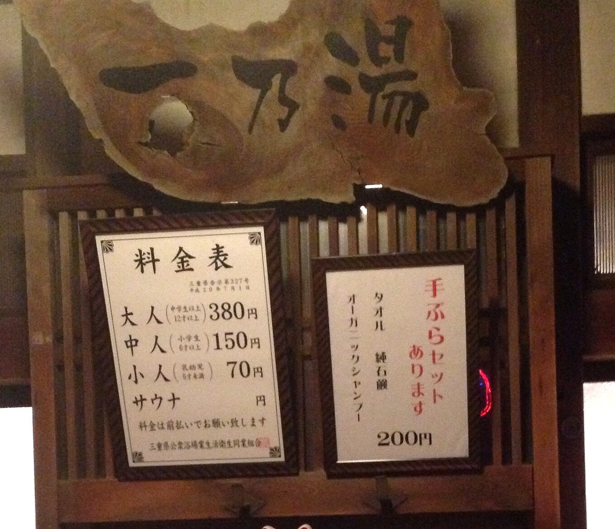 The framed price board above the entrance of Ichinoyu bathhouse in Iga, Mie, listing adult, middle and child fees in three lines with the prefectural notification number printed under the heading, beside a second notice offering a towel-and-soap set for 200 yen