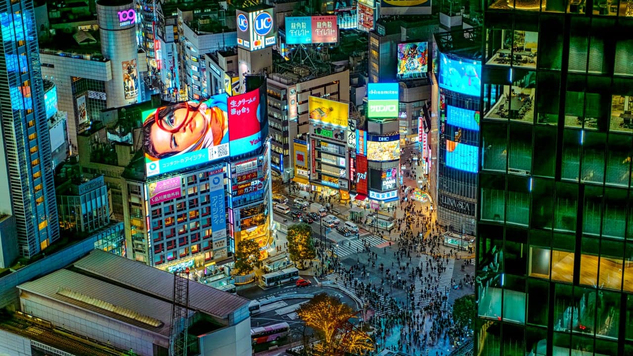 An aerial view of Shibuya Crossing at night, the famous scramble intersection alive with traffic and crowds