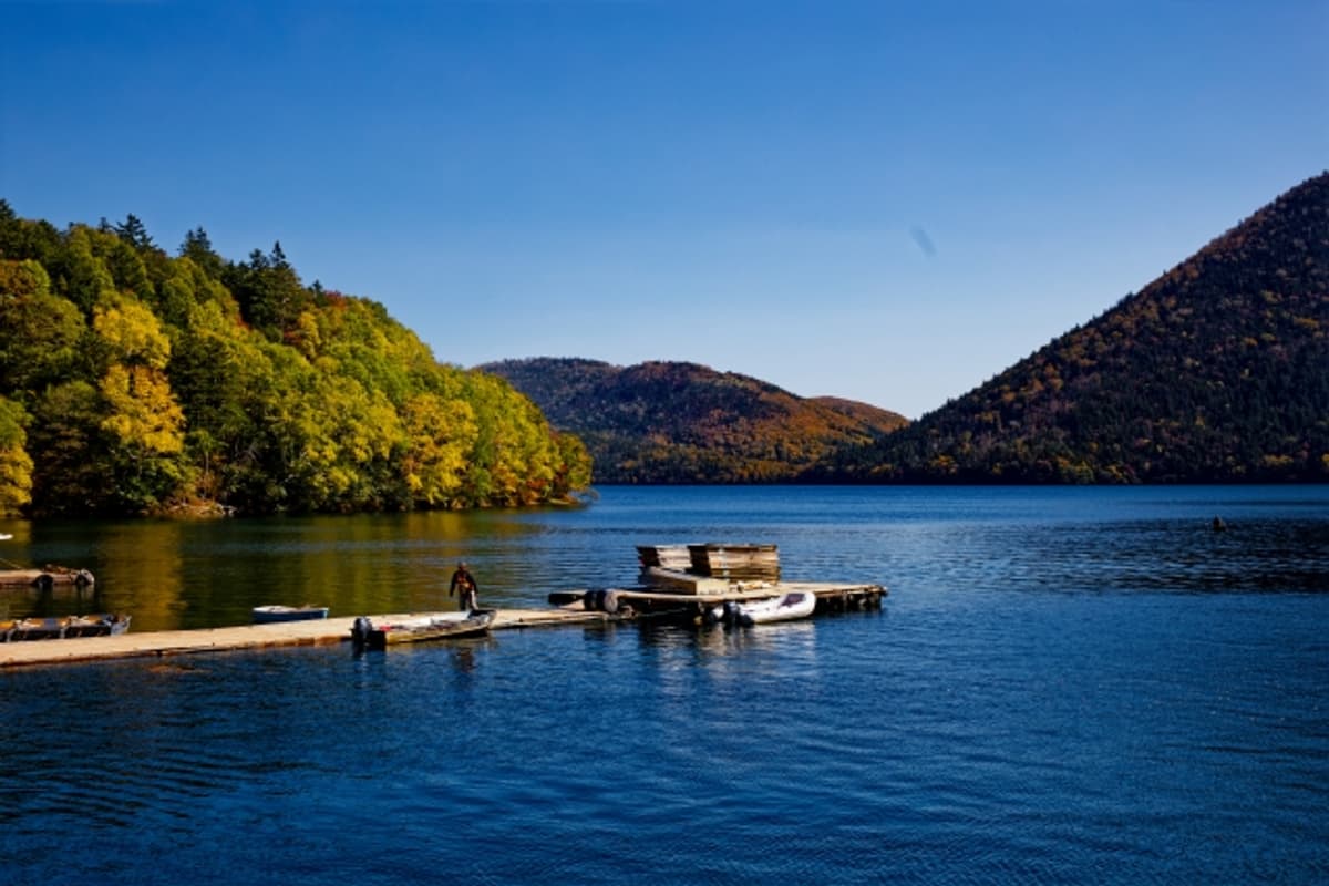Lake Shikaribetsu in autumn: red and gold foliage reflected on still water with layered mountain ridges behind