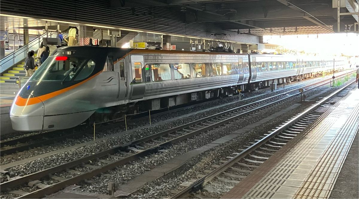 JR 岡山站月台旁停著一列 8000 系特急電車,銀色流線型車頭配橘色飾帶,車身是銀色不鏽鋼與一排車窗,前景是幾條鐵軌與月台邊的黃色導盲磚,左後方是通往月台的樓梯