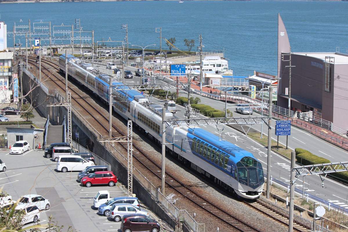 俯瞰島風號沿著鳥羽灣邊的鐵道駛來:藍白相間的車廂排成一長列,右側是海邊的道路與碼頭,遠處是藍色的海面