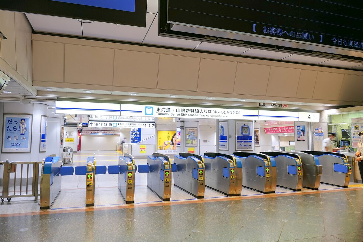 The Tokaido and Sanyo Shinkansen central transfer gates at Tokyo Station: a row of blue and silver automatic gates all showing green arrows, under a blue sign reading Tokaido, Sanyo Shinkansen Tracks (Central Entrance), with a Smart EX poster on the wall to the left and a staffed booth to the right, the floor empty of passengers