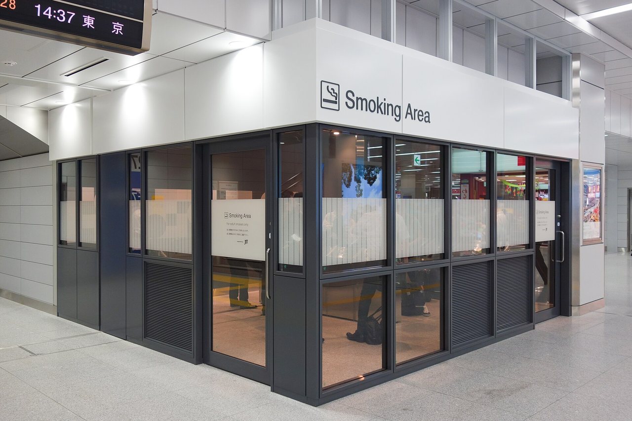 A glass-walled smoking room inside the Shinkansen gates at Shin-Osaka, signed Smoking Area with an adult-smokers-only notice on the door