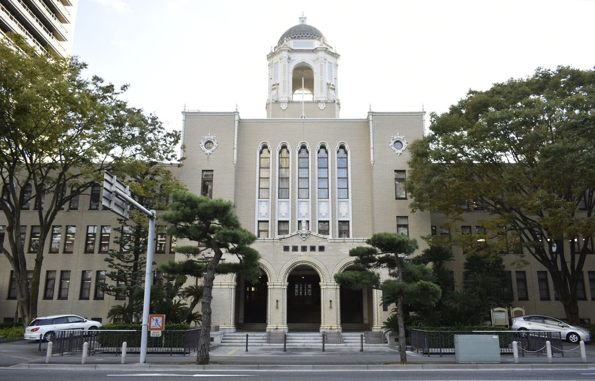 靜岡市役所靜岡廳舍本館正面:米色磚牆的三層西式建築,中央頂端是白色圓頂塔樓,下方三個拱形入口,門前兩側種著松樹