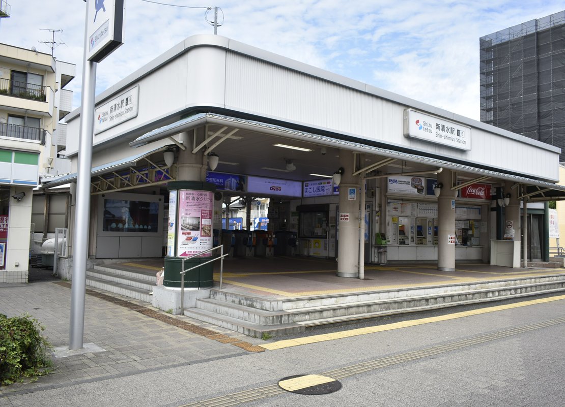 靜岡鐵道新清水站的平房站舍:白色弧形屋簷下掛著「新清水駅 Shin-shimizu Station」站名牌,屋簷下是自動剪票機與售票機,門前有幾階寬台階