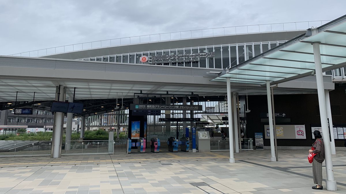 南町田グランベリーパーク站的グランベリーパーク口:大片玻璃屋頂下是一排自動剪票口,上方掛著「南町田グランベリーパーク駅 グランベリーパーク口」的招牌,站體外牆有東急標誌與站名,前面是石板廣場,右邊一位背對鏡頭的旅客,陰天