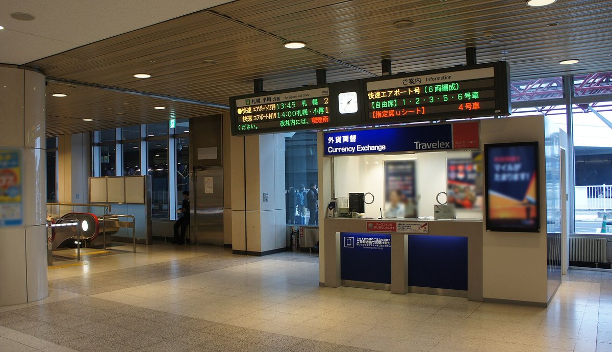 新千歲機場國內線到達大廳的 JR 發車看板，左邊列出往札幌・小樽方向的快速エアポート，右邊寫快速エアポート號 6 両編成、自由席 1・2・3・5・6 號車、指定席 u シート 4 號車，下方是外幣兌換櫃台