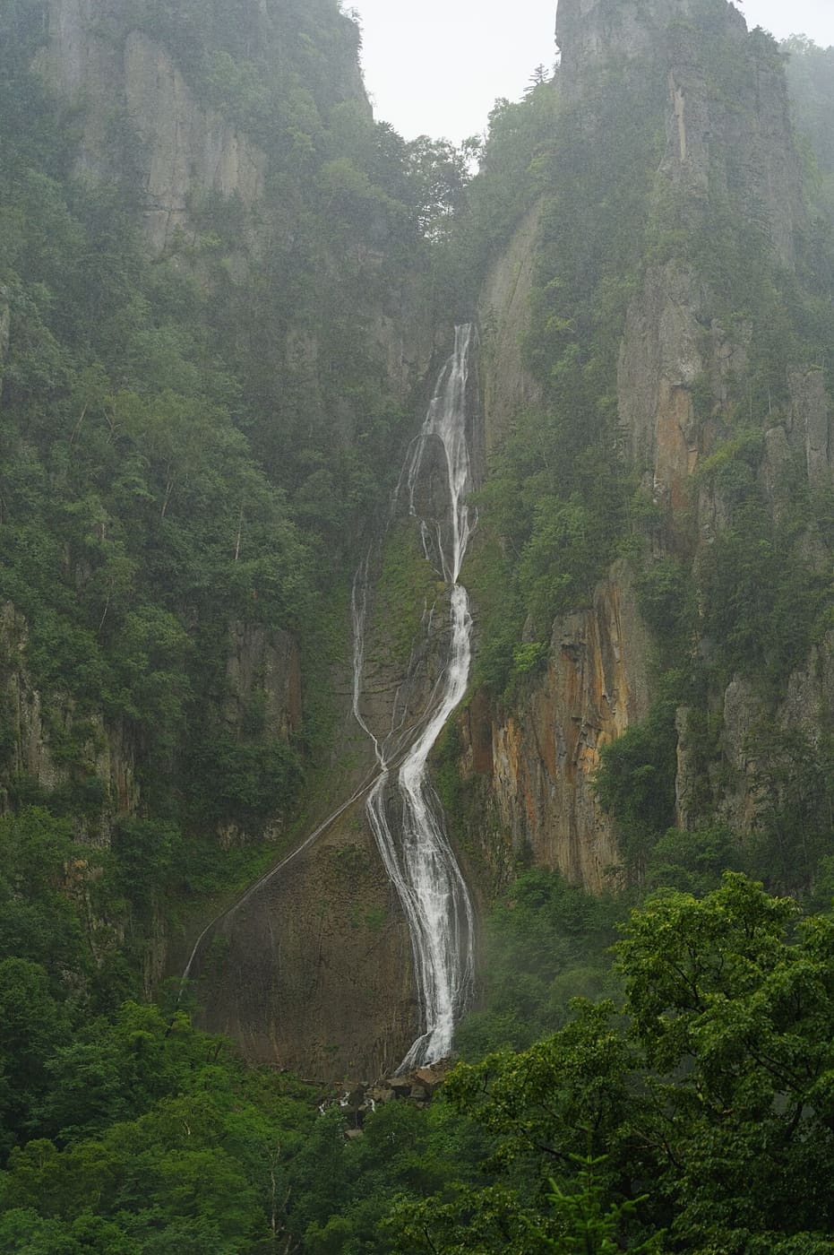 Ginga Falls in summer rain, thin strands of water sliding down a sheer cliff face at Sounkyo