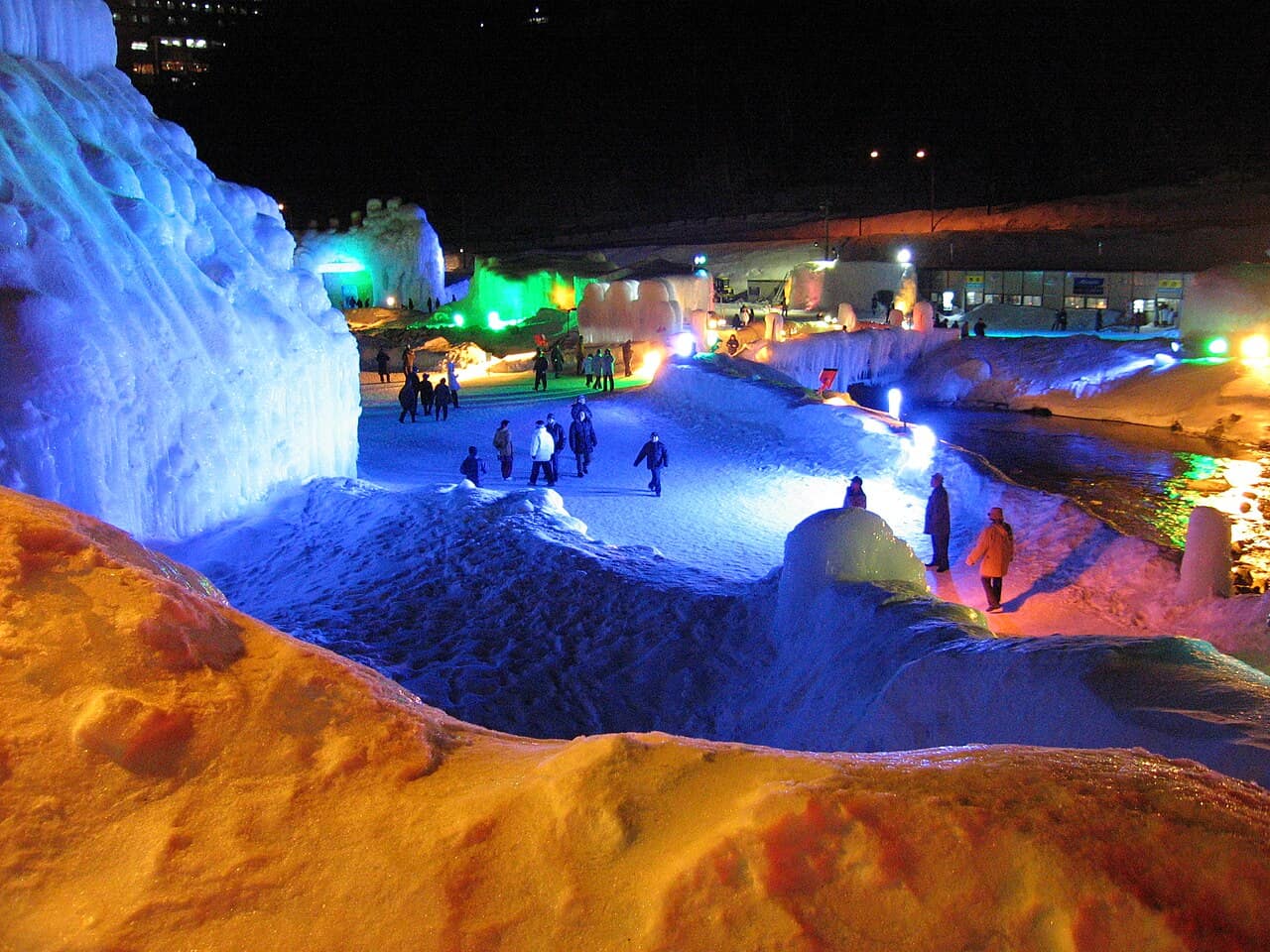 Sounkyo Ice Waterfall Festival grounds at night, with ice towers and snow paths lit in blue and orange
