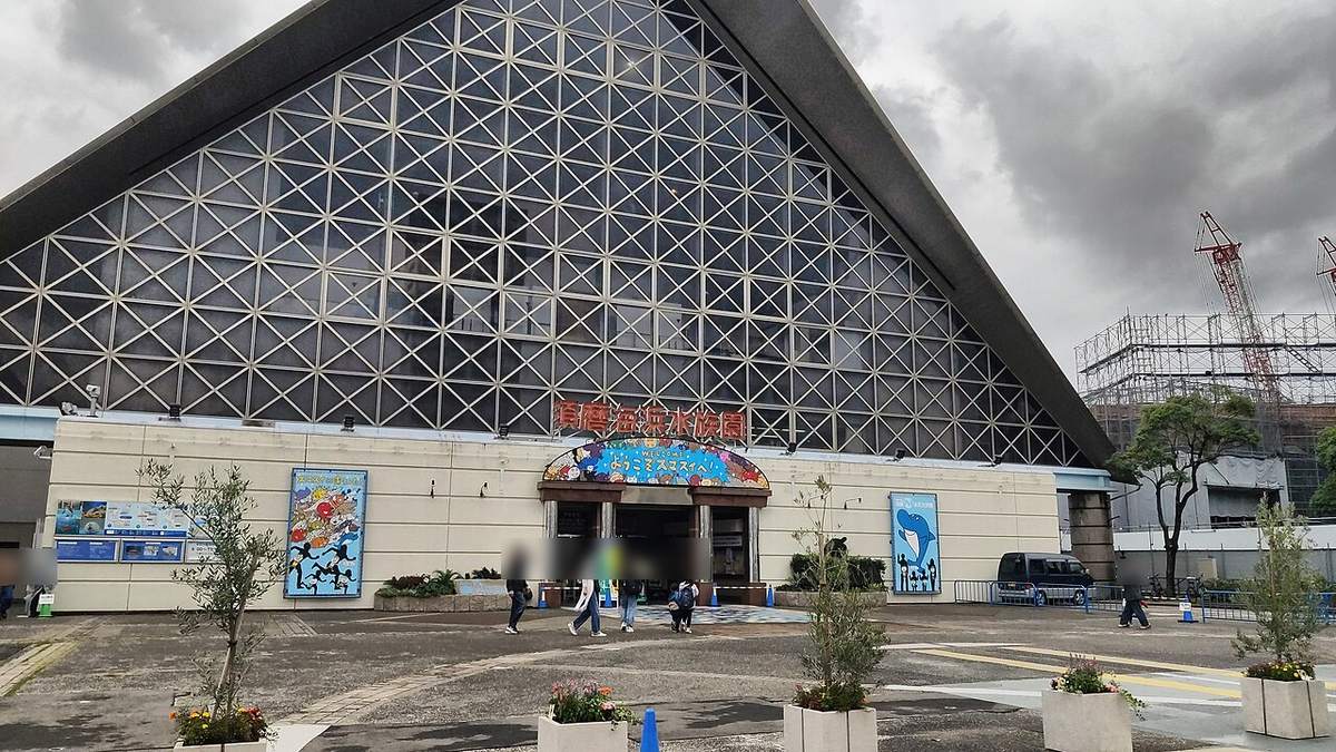 2022 年的舊須磨海浜水族園,三角形格子玻璃屋頂的大建築,正面紅字寫著須磨海浜水族園,入口拱門上是ようこそスマスイへ的彩色看板,右側看得到工地鷹架與起重機