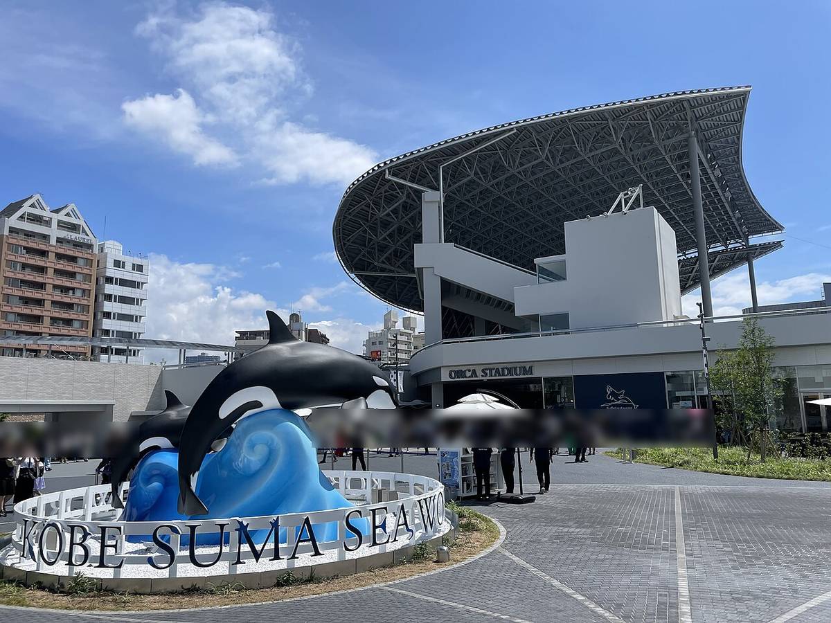 神戶須磨海洋世界的虎鯨館オルカスタディアム外觀,黑色鋼構大屋頂與白色樓梯塔,1 樓外牆有 ORCA STADIUM 字樣與深藍色的 Buffet restaurant BLUE OCEAN 招牌,前方廣場立著虎鯨雕像