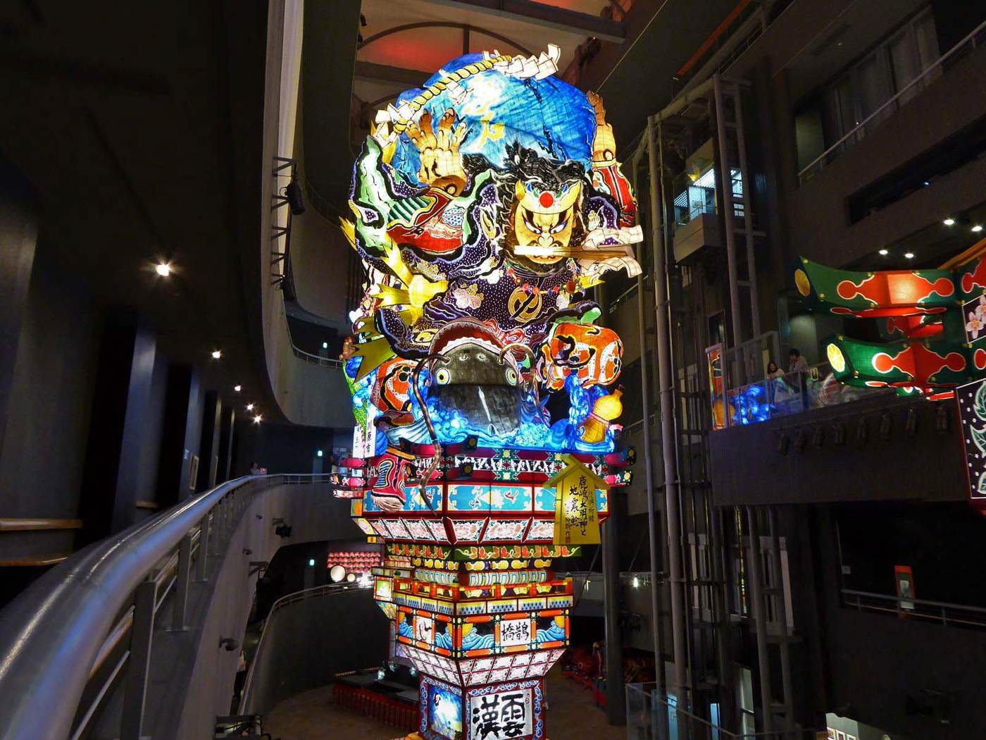 Interior of Tachineputa no Yakata, with visitors descending a spiral ramp beside a towering illuminated float