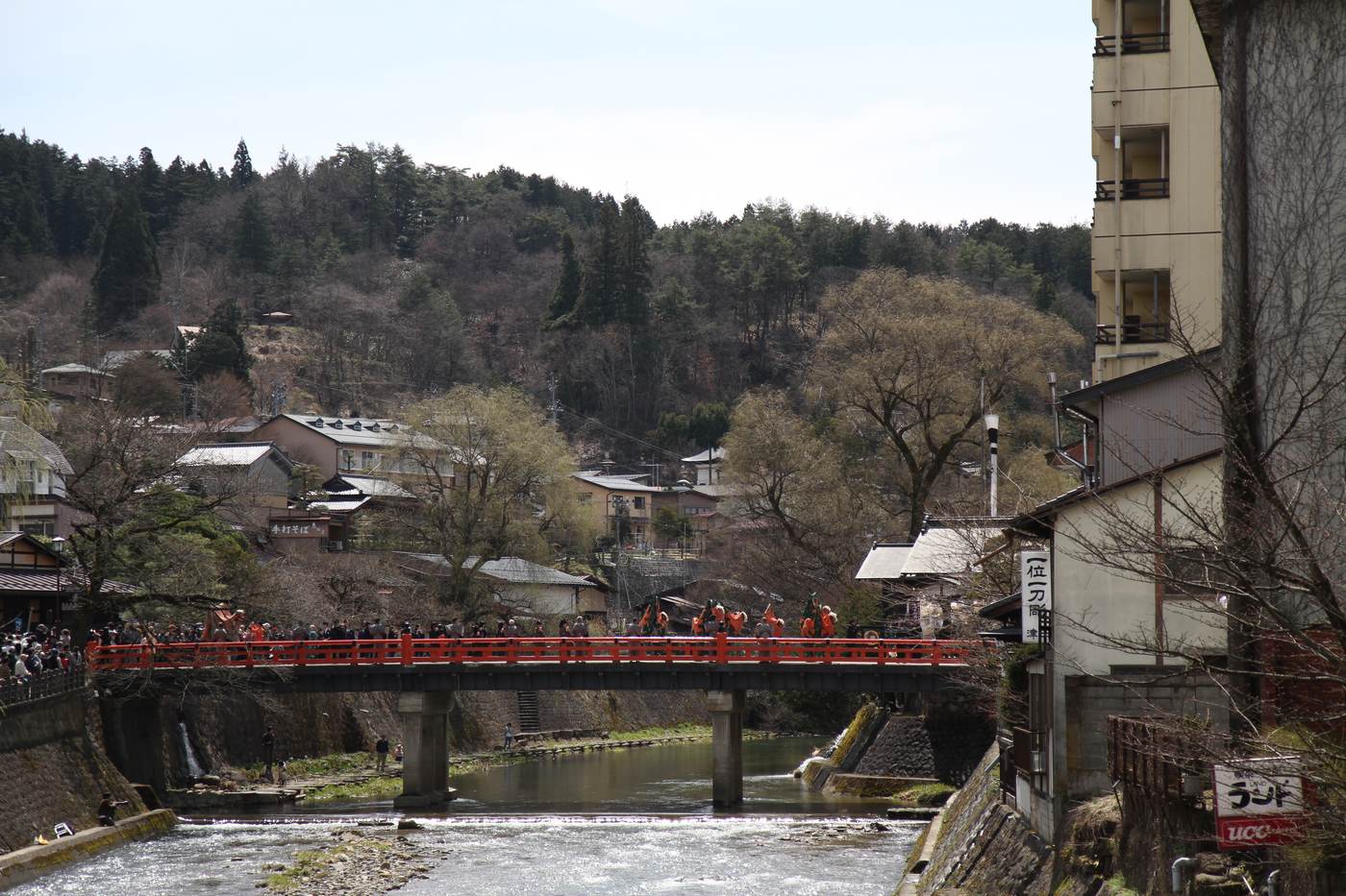 The vermilion Nakabashi bridge over the Miyagawa river in Takayama with a festival procession crossing it