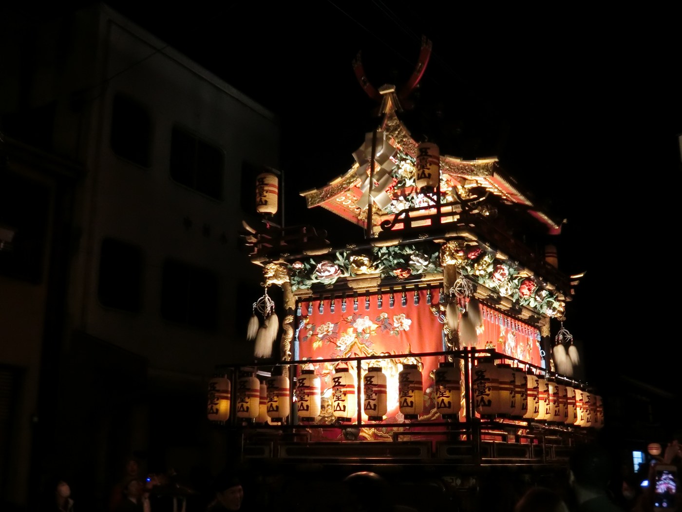 A Takayama Festival float at night, ringed with rows of glowing paper lanterns against a black sky