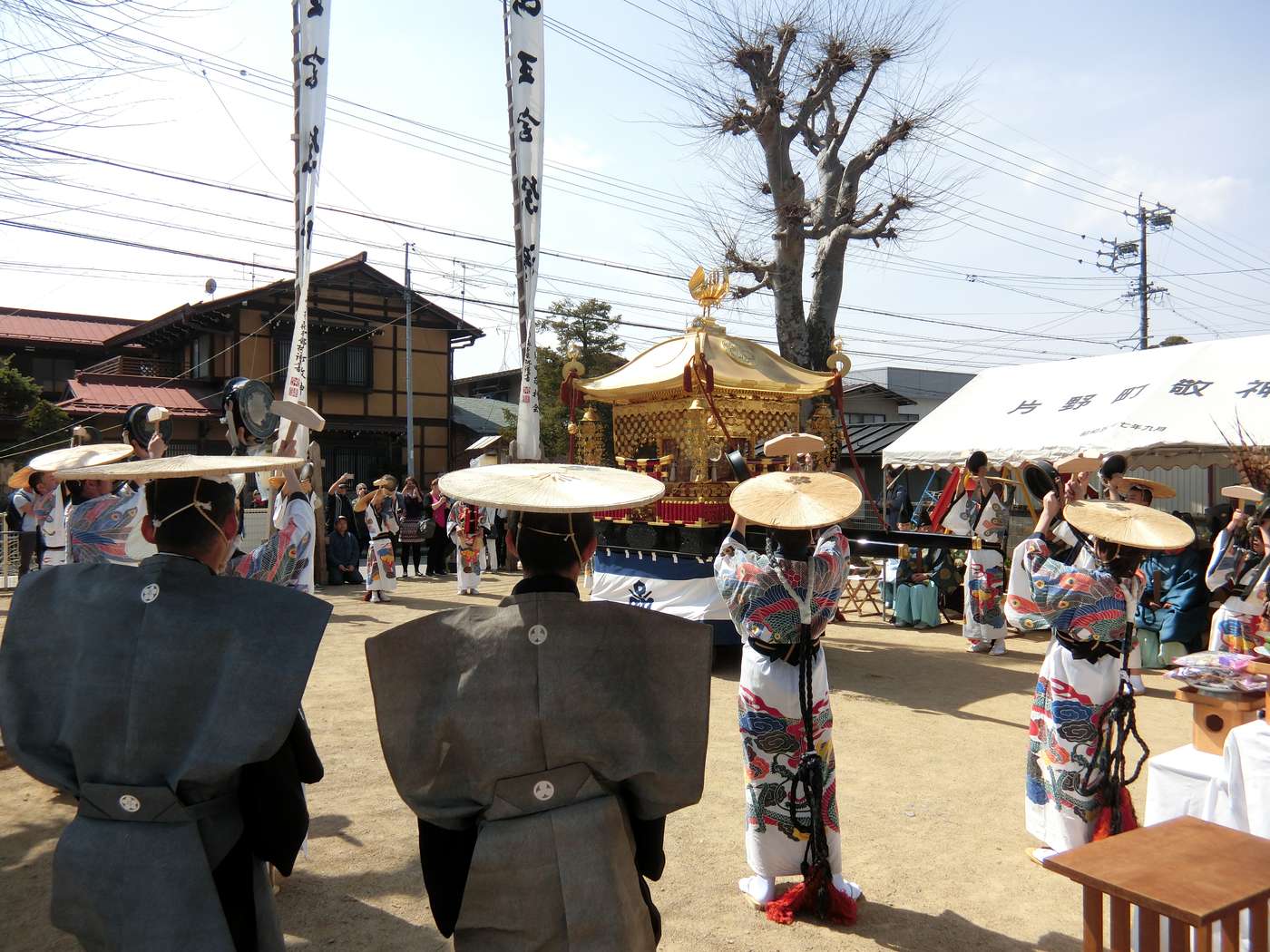 Togeiraku performers in formal kamishimo and wide straw hats, holding gold hand-gongs in a procession line