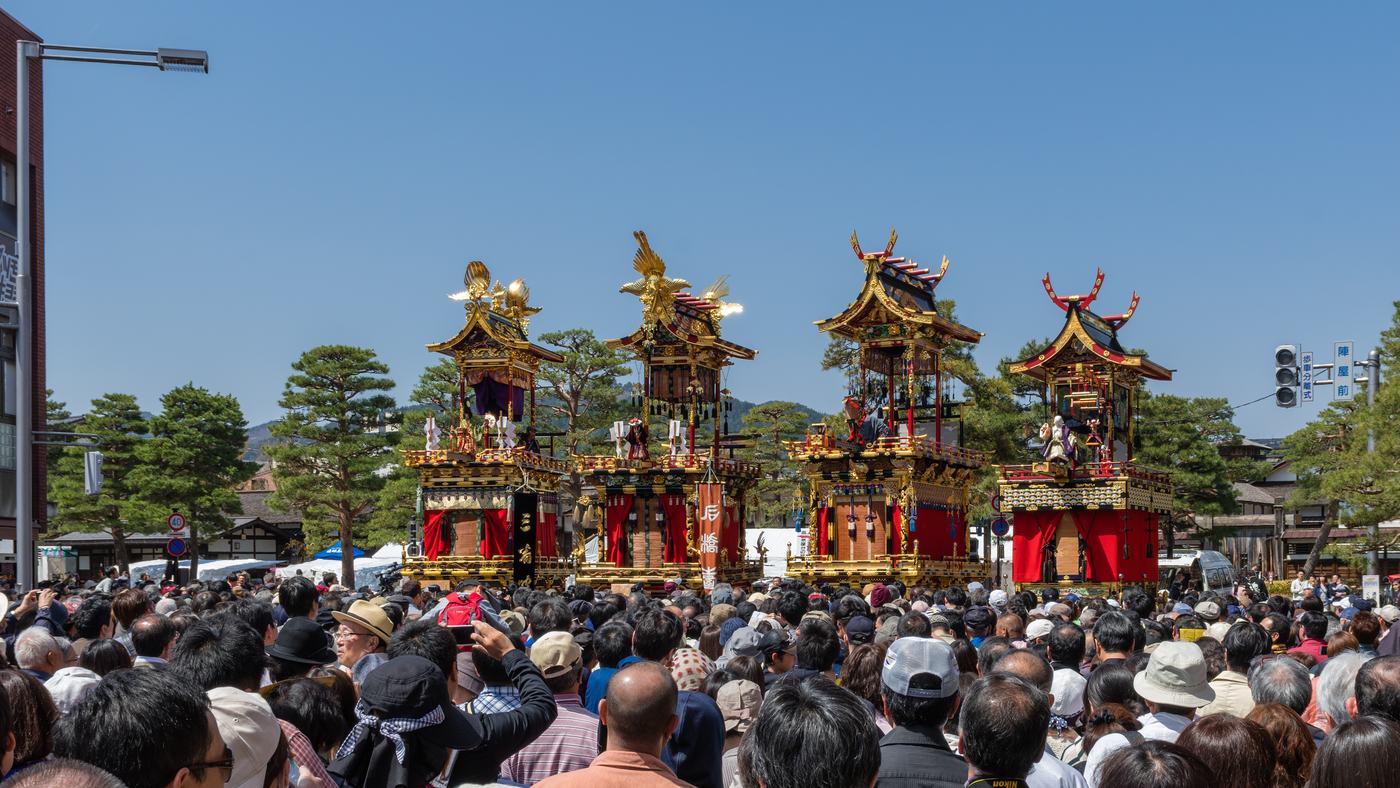 Four Takayama Festival floats displayed side by side above a dense standing crowd holding up phones