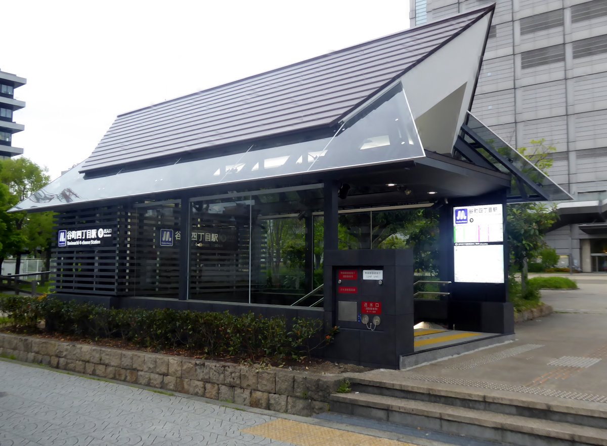 谷町四丁目站 9 號出入口:黑色格柵牆加斜屋頂的地面出入口建築,牆上有 Osaka Metro 標誌和「谷町四丁目駅」站名,右側是往下的樓梯