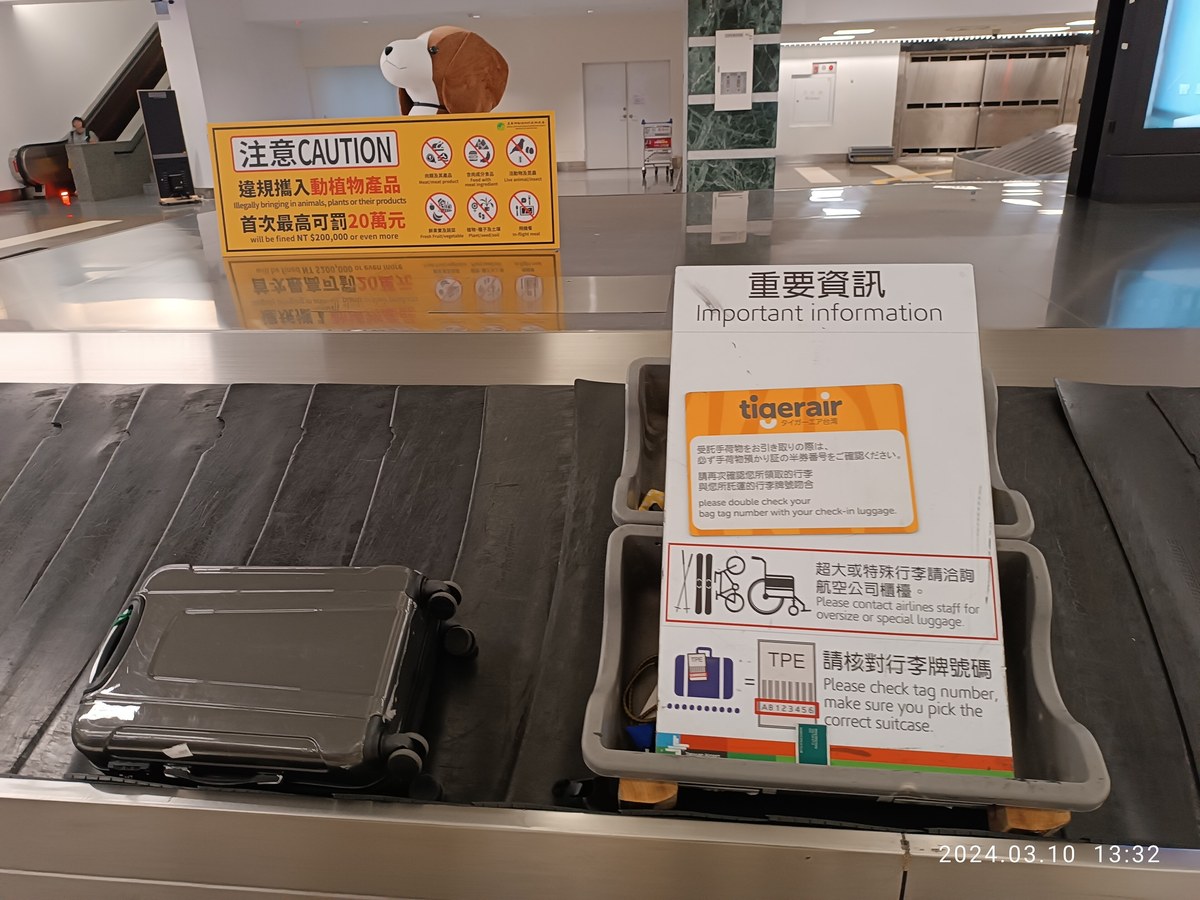 Yellow quarantine warning board standing on a baggage carousel at Taoyuan Airport, reading that illegally bringing in animals, plants or their products will be fined NT$200,000 or even more, with a beagle mascot figure behind it
