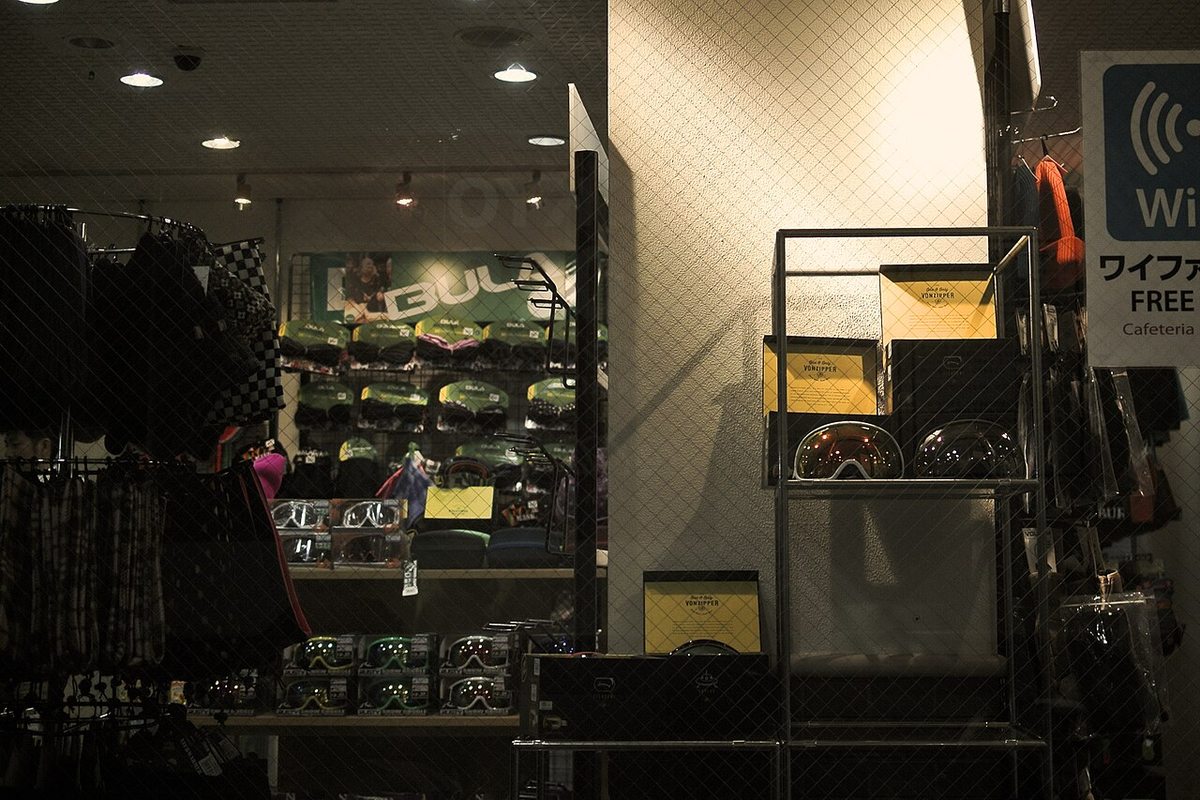 Shelves inside a shop at Sapporo Teine stacked with boxed goggles, beanies and neck warmers, a Japanese free Wi-Fi and Cafeteria sign at the top right