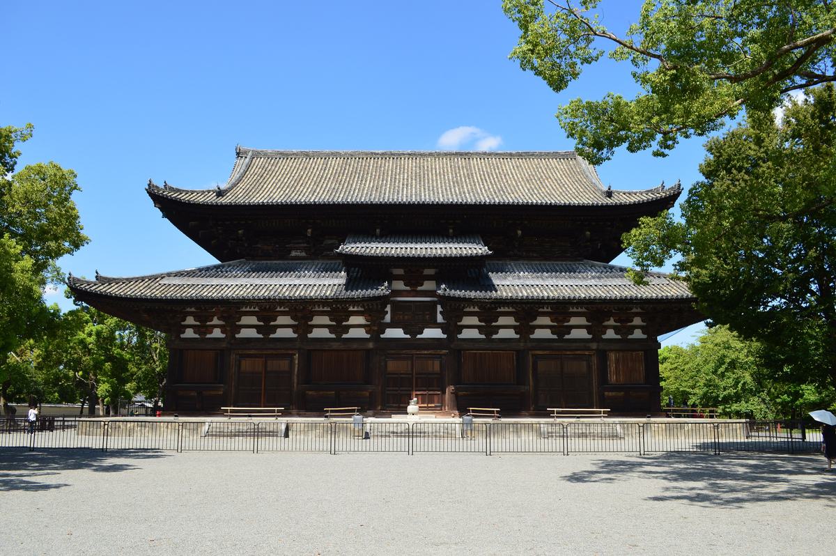 東寺金堂正面外觀:兩層屋簷的深色木造大殿,前方是欄杆與碎石廣場,白天晴空