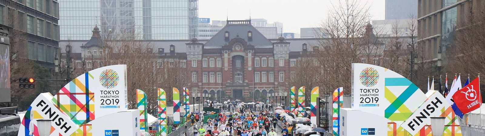 東京馬拉松終點:行幸通上兩座寫著 FINISH 的彩色拱門,正後方是紅磚的東京站丸之內站舍,賽道兩側有圍欄,觀眾撐傘站在圍欄外