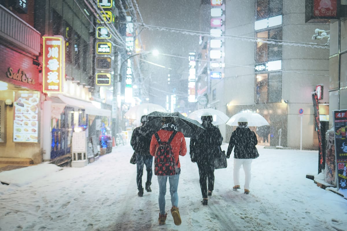 Snow falling on Kabukicho in Shinjuku on 22 January 2018, pedestrians under umbrellas walking on a snow-covered street beneath lit neon signs