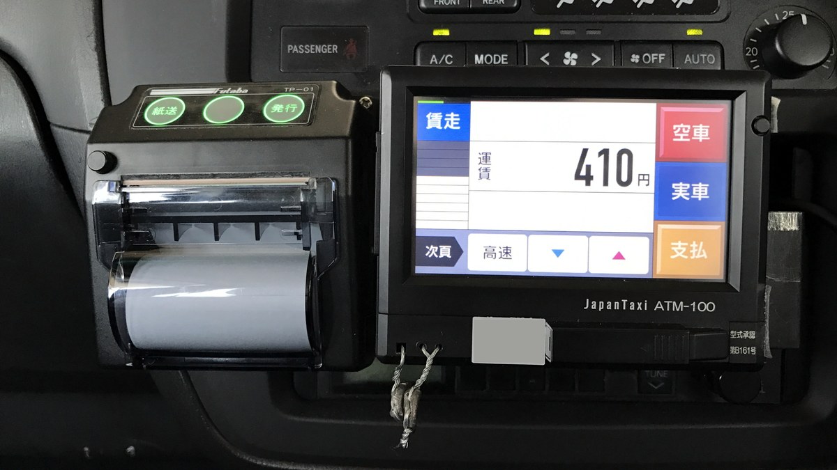 A JapanTaxi ATM-100 fare meter and receipt printer inside a Japanese taxi, the screen reading 410 yen beside the vacant, hired and payment keys