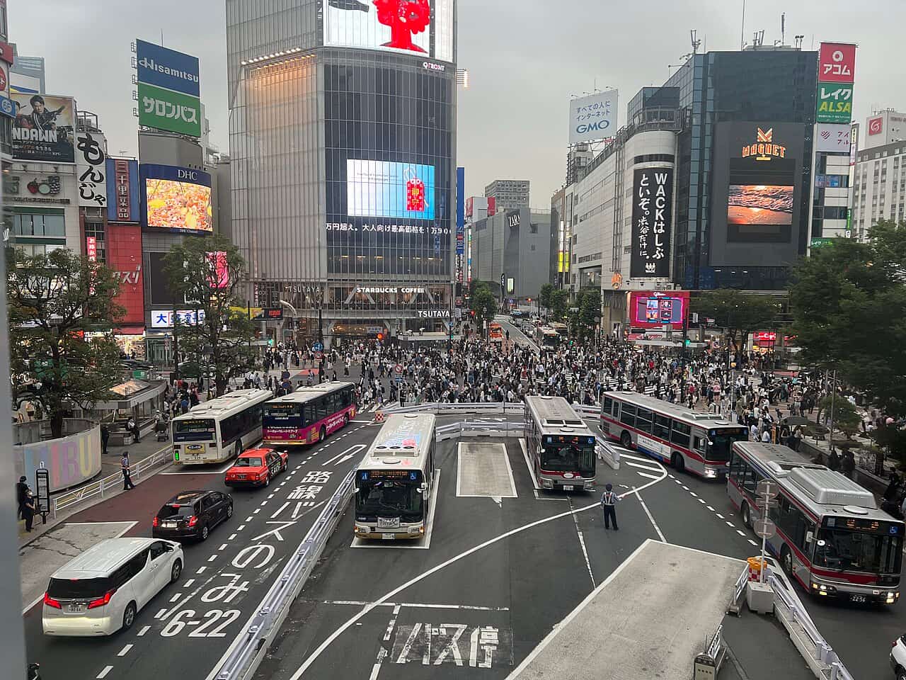 東京澀谷十字路口擠滿穿越馬路的人潮，四周是高樓與霓虹廣告牆