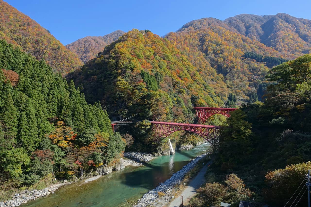 黑部峽谷的紅色拱橋與翡翠色溪水，托盤車行駛其上