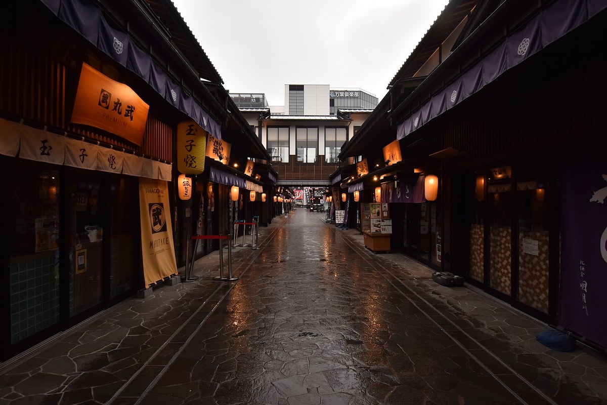 The Edo-style timber arcade of Toyosu Menuki Odori at Senkyaku Banrai, noren curtains, paper lanterns and tamagoyaki shop signs lining a flagstone lane still shuttered at dawn