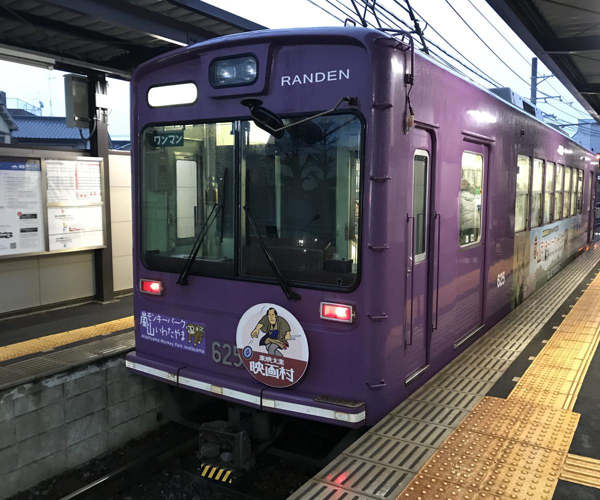 嵐電撮影所前站月台邊的紫色 625 號電車,車頭掛著圓形頭標,畫著拔刀的武士、下方寫「東映太秦 映画村」,左邊另貼「嵐山モンキーパーク いわたやま」的廣告