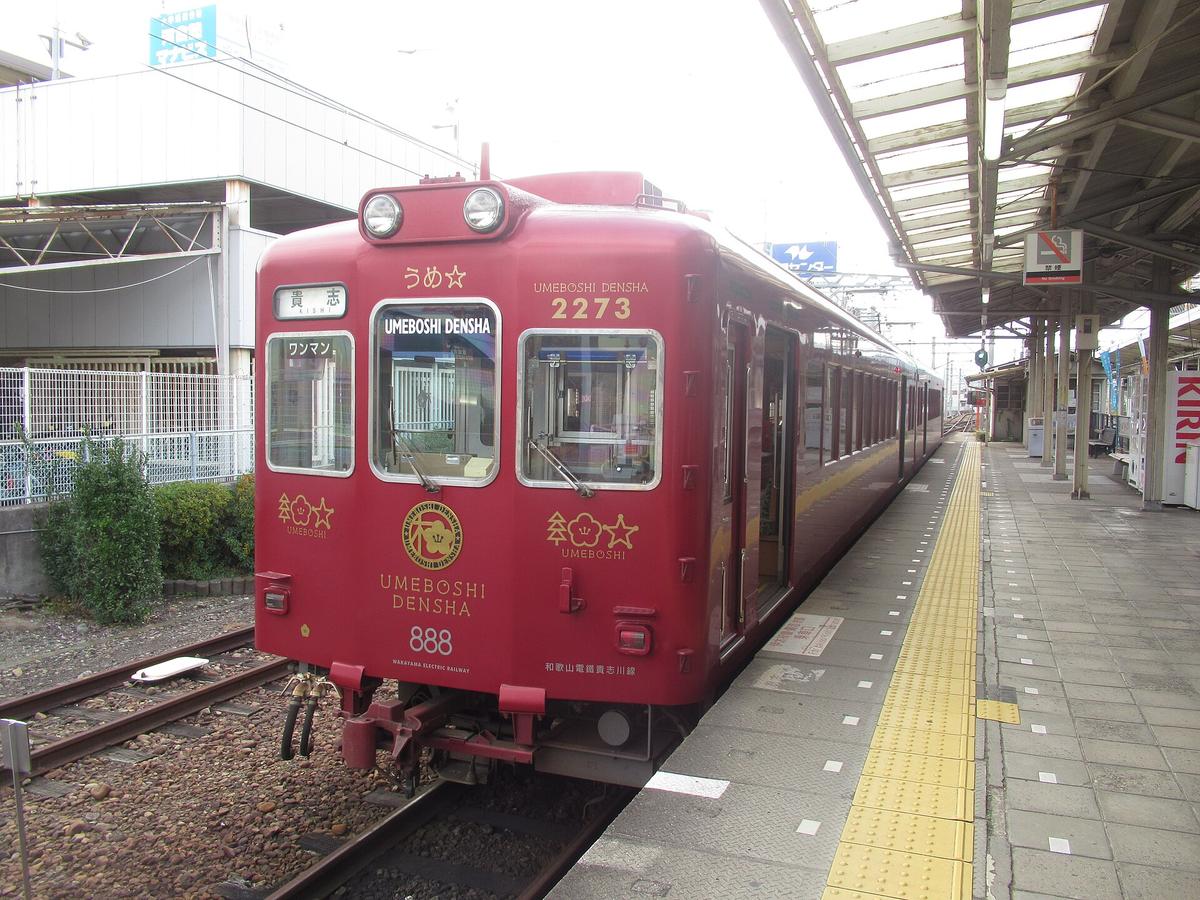 停在和歌山站月台的うめ星電車:整台暗紅色車身,車頭寫 UMEBOSHI DENSHA 2273、「うめ☆」和行先牌「貴志」,正面有金色梅花圓形徽章和「888」數字,右邊是有頂棚的月台與黃色導盲磚