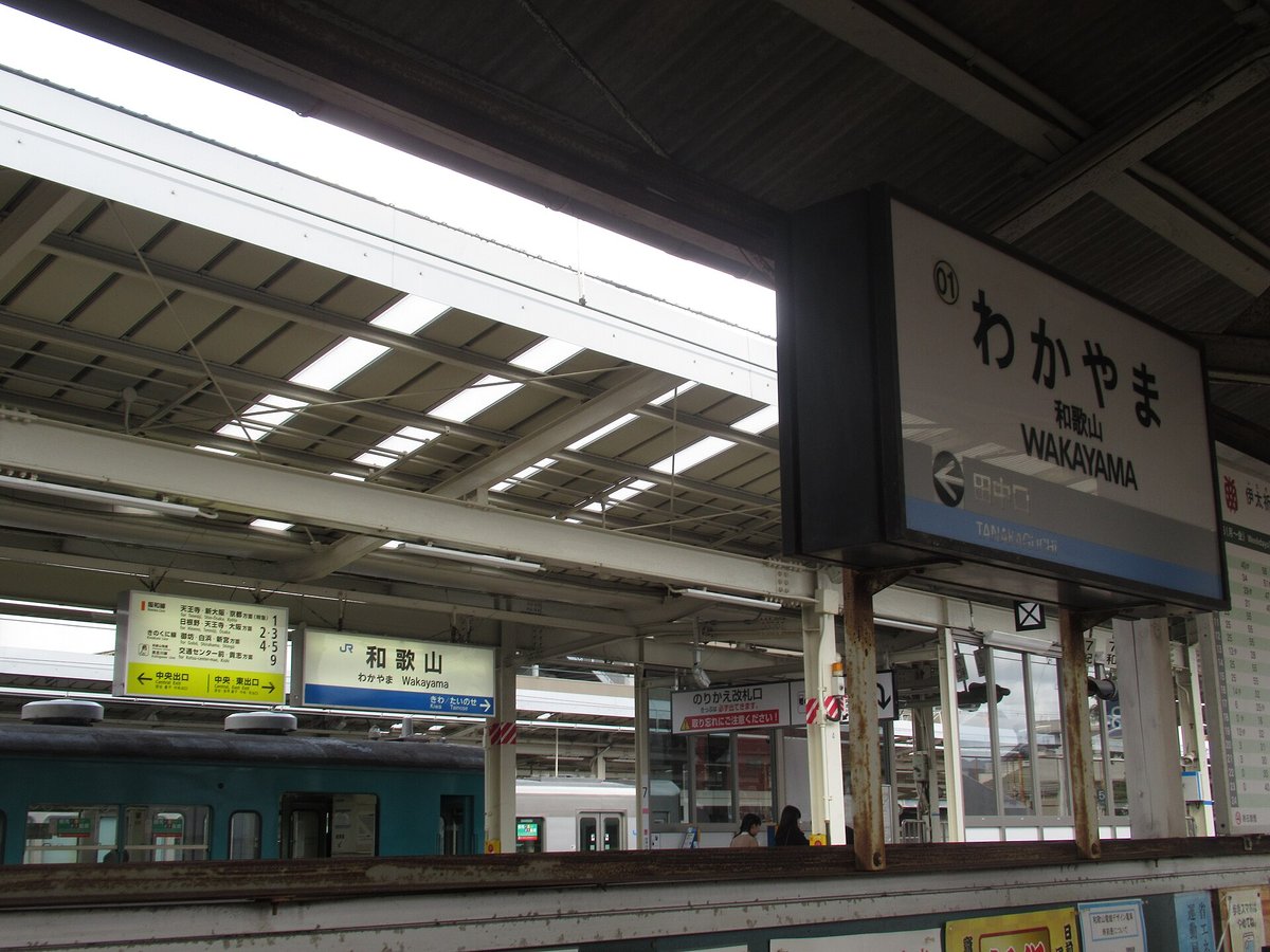 和歌山站月台頂棚下的站名牌:右邊是貴志川線的「01 わかやま 和歌山 WAKAYAMA」,左箭頭指下一站田中口;左下是 JR 的「和歌山」站名牌,旁邊黃綠色看板列出各線月台,最下一列「貴志川線 交通センター前・貴志方面 9」,底下黃色條是中央出口、中央・東出口的方向;中間紅白牌子寫「のりかえ改札口」