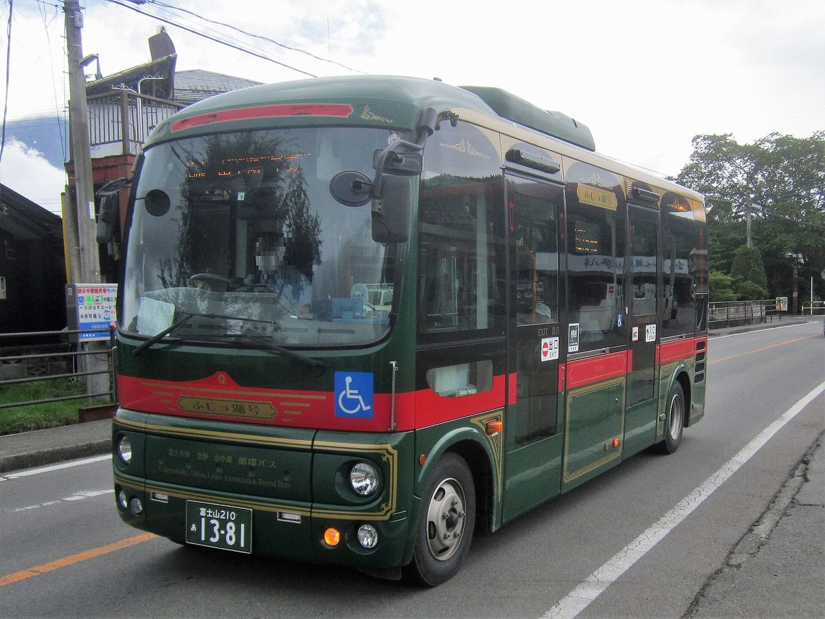 墨綠車身配紅色腰線的小型巴士開在路上，車頭和車側的金框牌子寫「ふじっ湖号」，車頭下方寫「富士吉田 忍野 山中湖 循環バス」，駕駛的臉已打馬賽克