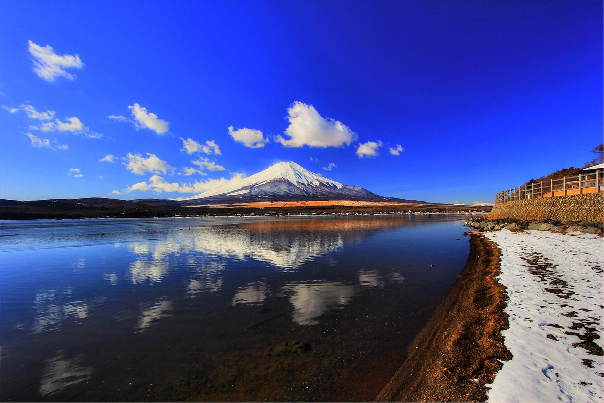 1 月長池親水公園一帶的湖岸：無風的湖面清楚倒映雪頂富士山和白雲，右邊岸上有殘雪，石砌護岸上架著木柵
